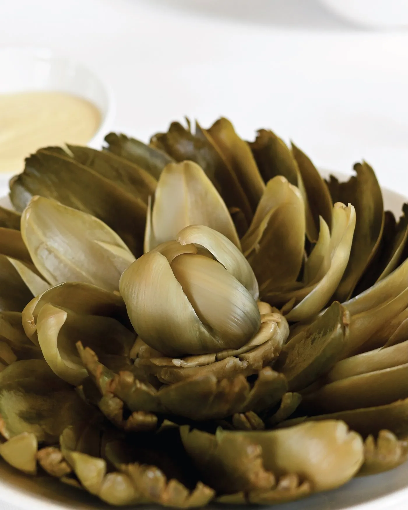 Alcachofa entera abierta como una flor, con vinagreta al lado