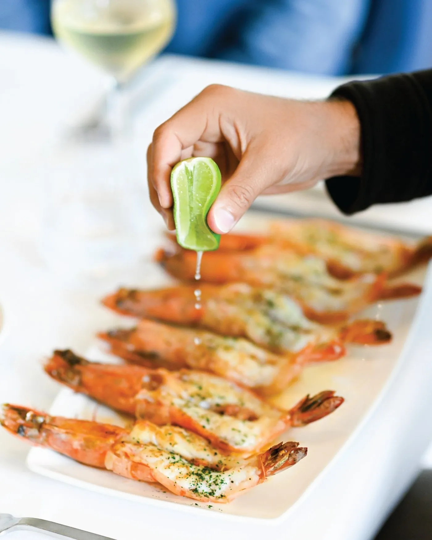 Una mano exprime limón sobre camarones al vino blanco en una bandeja alargada