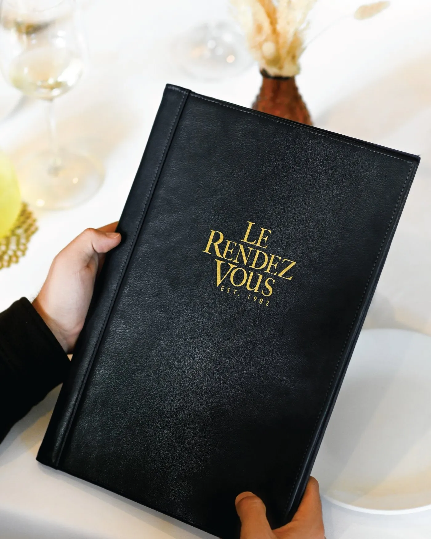 Manos abriendo la carta de Le Rendez Vous, un libro negro con letras doradas