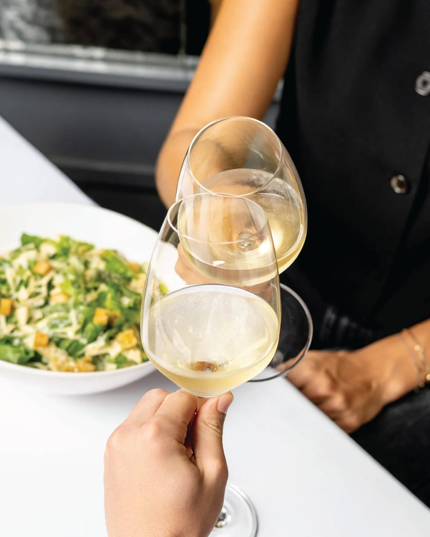 Brindis con copas de vino blanco sobre una ensalada en la mesa