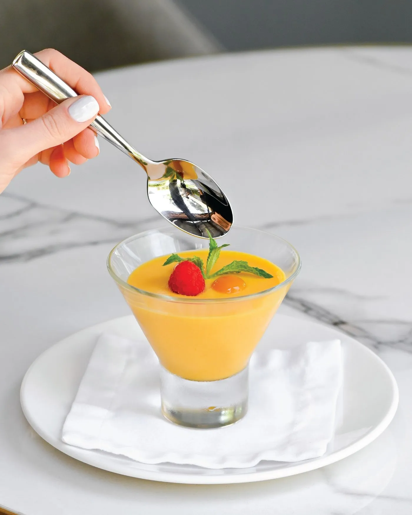 Una cuchara toma mousse de mango de una copa con una fresa