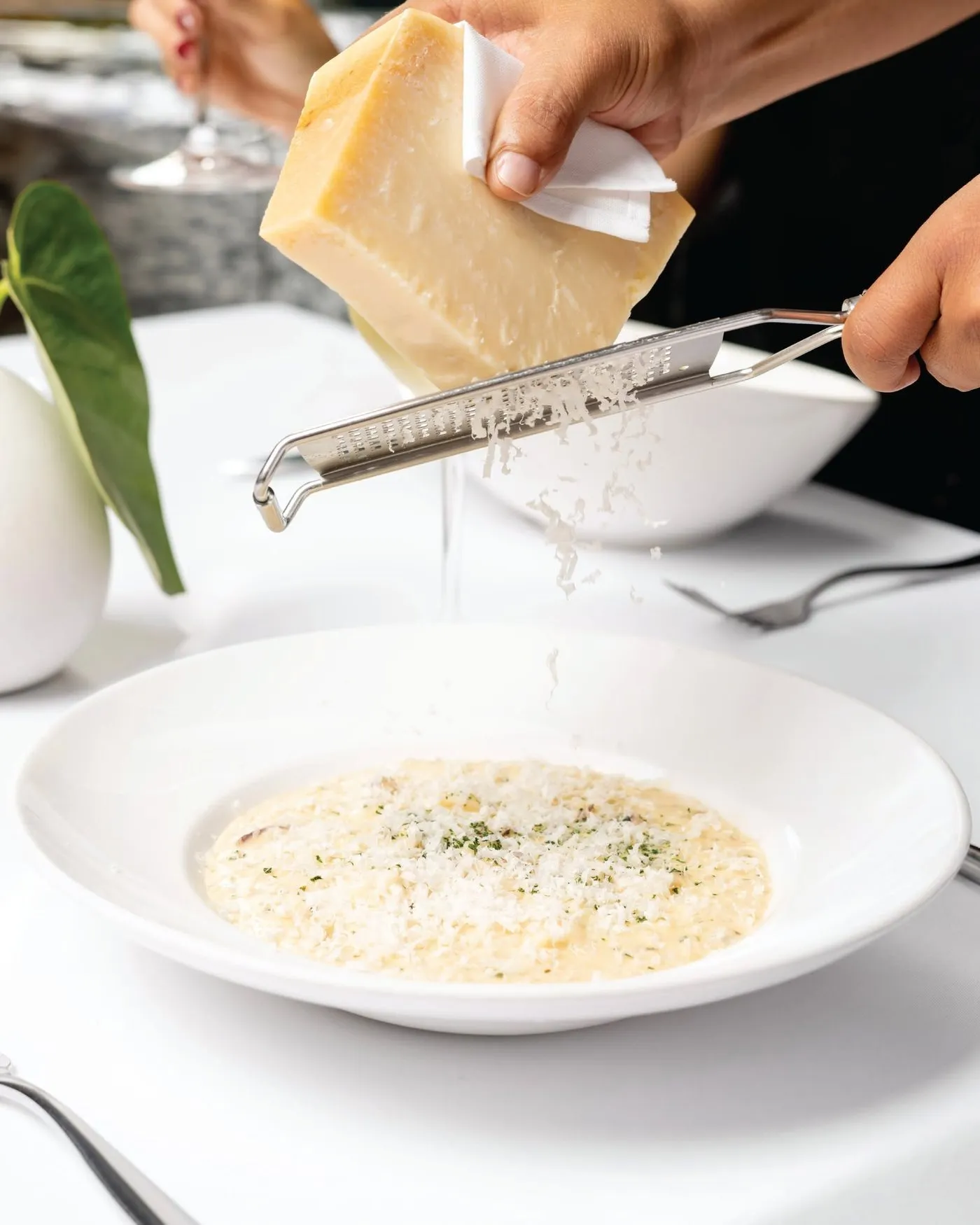 Un mesero ralla parmesano sobre un risotto de calamares