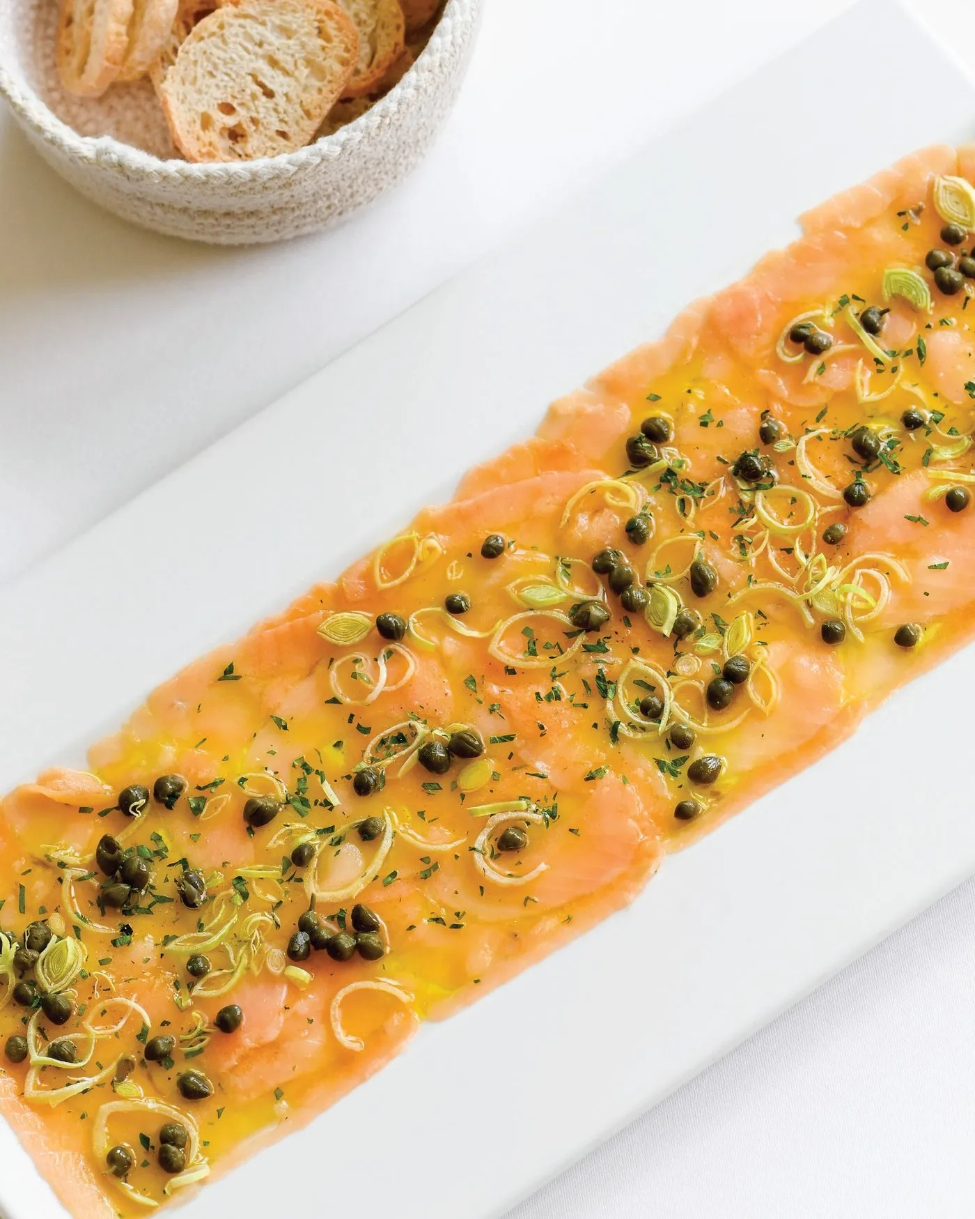 Láminas finas de salmón con alcaparras y cebollín en un plato blanco alargado